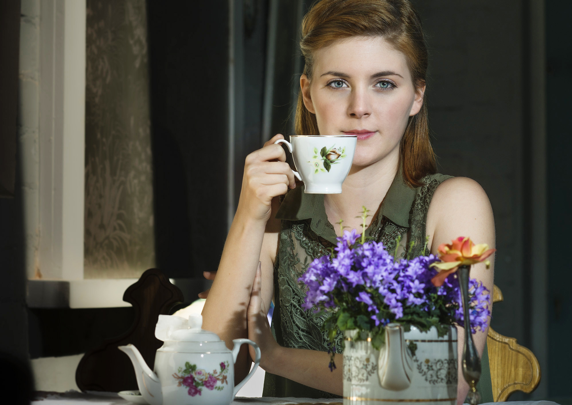 Colour photographic portrait of female drinking tea looking into camera.